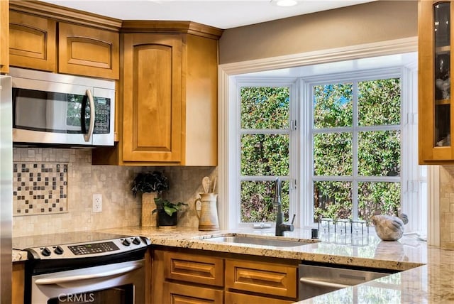 kitchen with decorative backsplash, brown cabinetry, appliances with stainless steel finishes, light stone countertops, and a sink