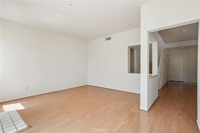 empty room with baseboards, visible vents, and light wood finished floors