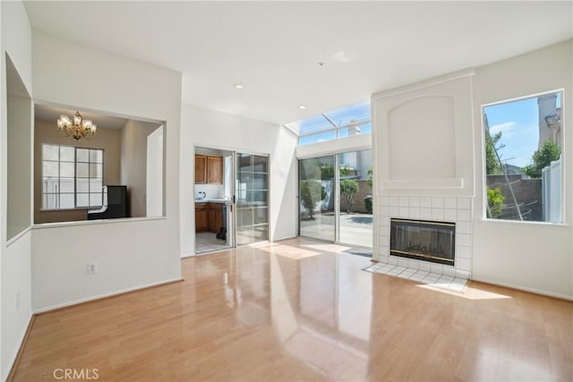 unfurnished living room with an inviting chandelier, plenty of natural light, wood finished floors, and a tile fireplace