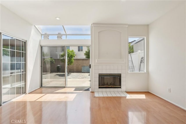 unfurnished living room with baseboards, a tiled fireplace, and wood finished floors