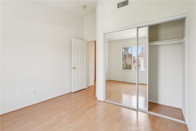 unfurnished bedroom featuring baseboards, a closet, wood finished floors, and visible vents
