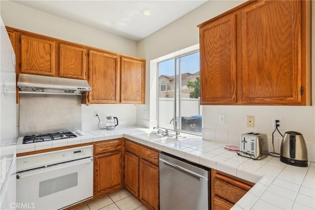 kitchen featuring a sink, brown cabinets, under cabinet range hood, and white appliances