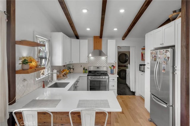 kitchen featuring stacked washer / dryer, appliances with stainless steel finishes, a sink, light countertops, and wall chimney exhaust hood