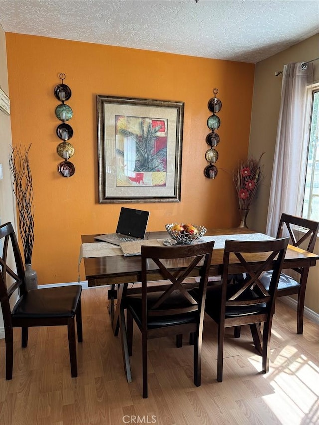 dining space with a textured ceiling, baseboards, and light wood-style floors