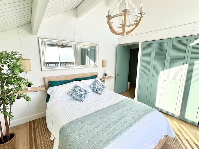 bedroom featuring a closet, lofted ceiling with beams, wood finished floors, and a notable chandelier