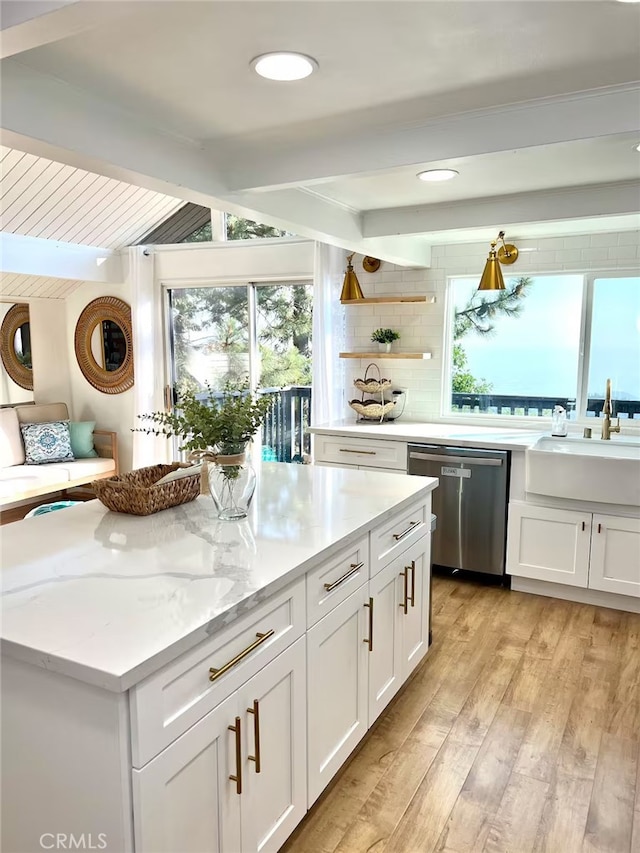 kitchen featuring stainless steel dishwasher, a sink, white cabinetry, and plenty of natural light