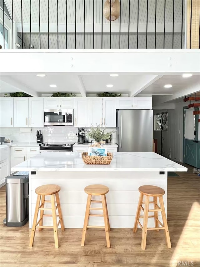 kitchen with a breakfast bar area, white cabinetry, tasteful backsplash, light wood finished floors, and stainless steel appliances