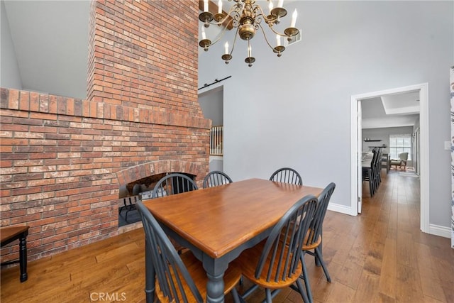 dining area featuring wood-type flooring, a fireplace, baseboards, a high ceiling, and a notable chandelier