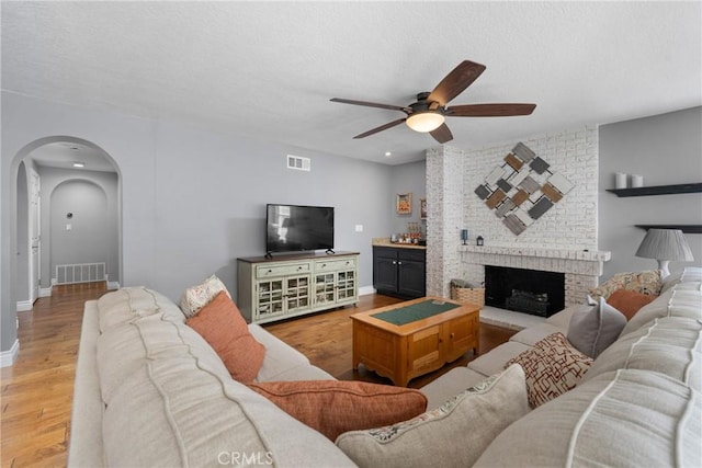 living area with arched walkways, a ceiling fan, wood finished floors, and visible vents