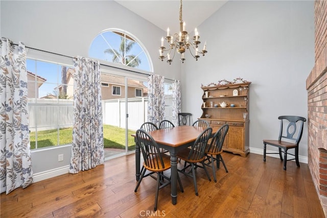 dining room with an inviting chandelier, baseboards, high vaulted ceiling, and hardwood / wood-style floors