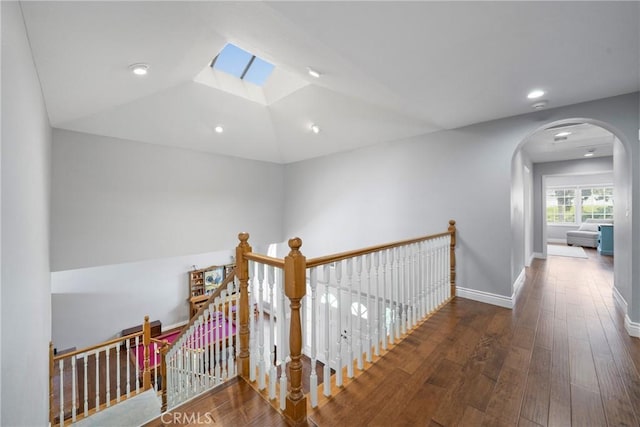 corridor featuring arched walkways, lofted ceiling with skylight, wood finished floors, and an upstairs landing