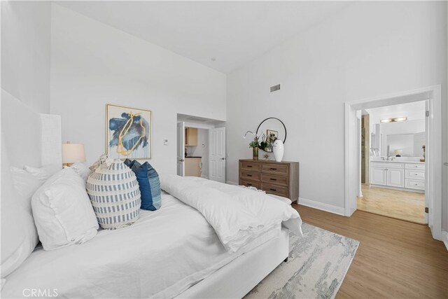 bedroom featuring connected bathroom, high vaulted ceiling, baseboards, wood finished floors, and visible vents