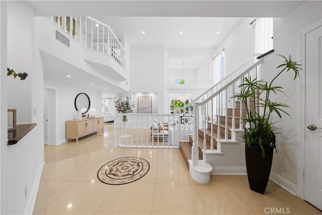 tiled entrance foyer with stairs, a high ceiling, visible vents, and baseboards