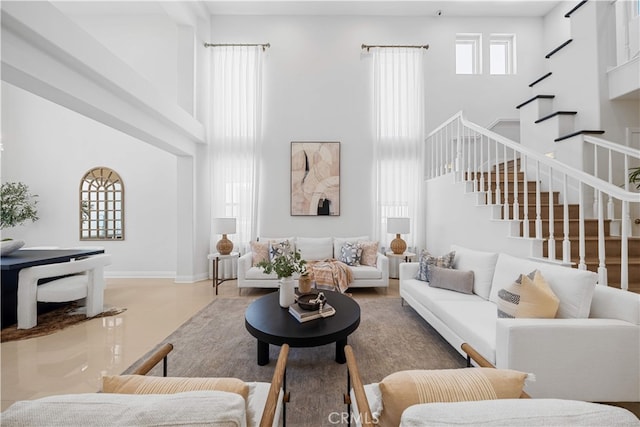 living area with stairway, baseboards, and a towering ceiling