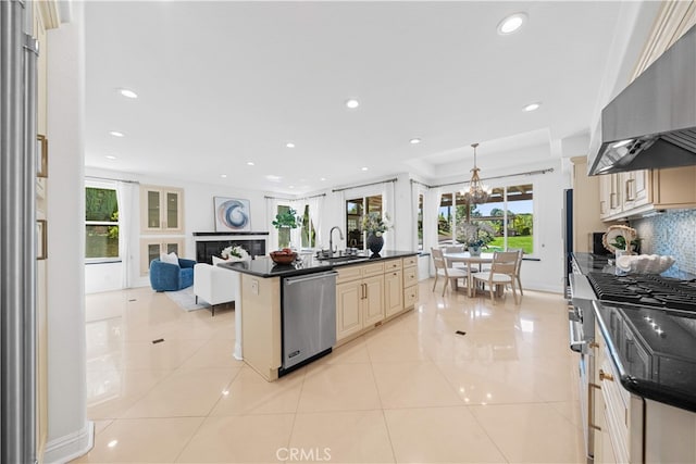 kitchen featuring cream cabinets, an inviting chandelier, a sink, dishwasher, and wall chimney exhaust hood