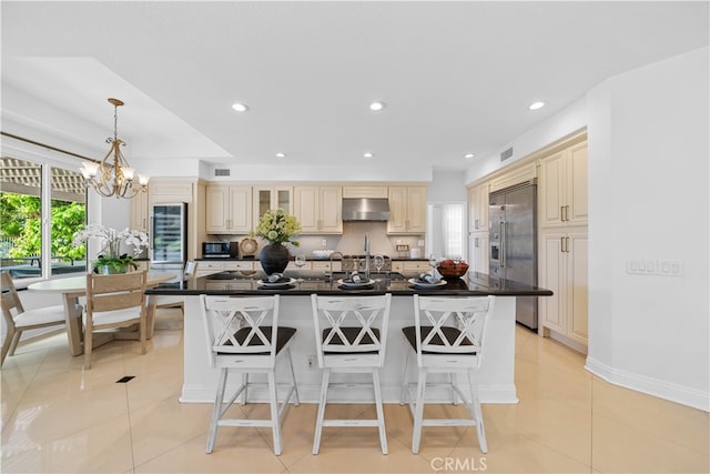 kitchen with stainless steel built in fridge, dark countertops, exhaust hood, and a breakfast bar area