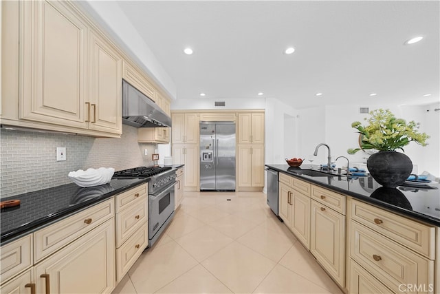 kitchen featuring ventilation hood, a sink, high end appliances, cream cabinetry, and tasteful backsplash