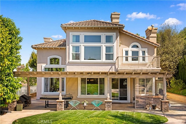 back of house with a patio area, stucco siding, a tiled roof, and a chimney