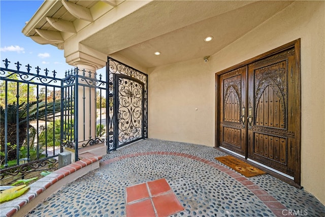 entrance to property featuring a gate, stucco siding, french doors, and fence