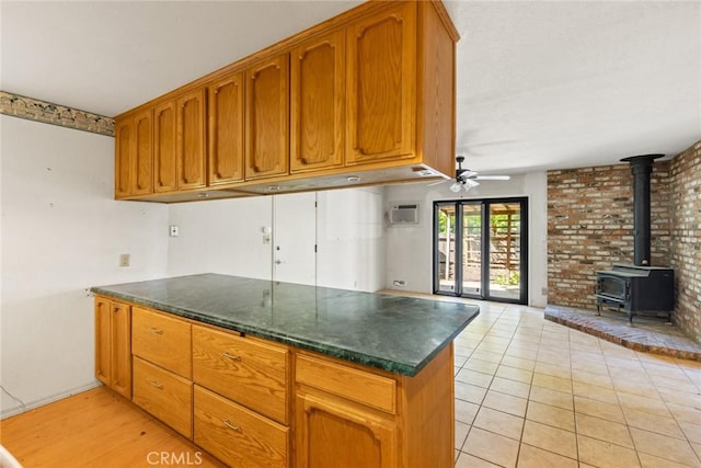 kitchen featuring brown cabinetry, a wood stove, a peninsula, open floor plan, and a ceiling fan