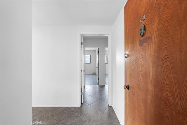 corridor featuring baseboards and dark tile patterned floors
