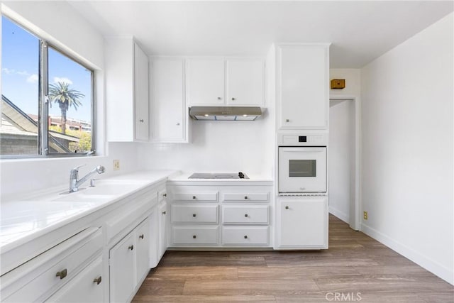 kitchen with a sink, black electric cooktop, white cabinetry, under cabinet range hood, and white oven