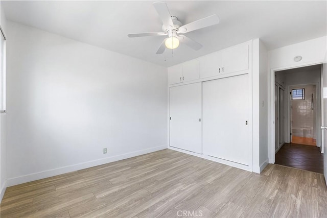 unfurnished bedroom featuring baseboards, ceiling fan, light wood finished floors, and a closet