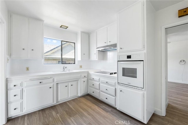 kitchen with under cabinet range hood, oven, white cabinets, and a sink