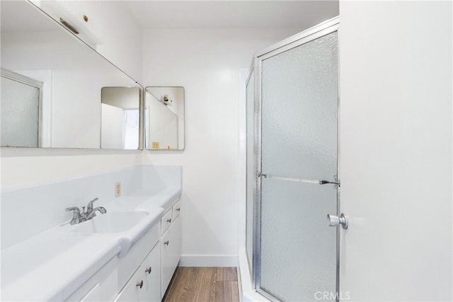 bathroom featuring baseboards, a shower stall, wood finished floors, and vanity
