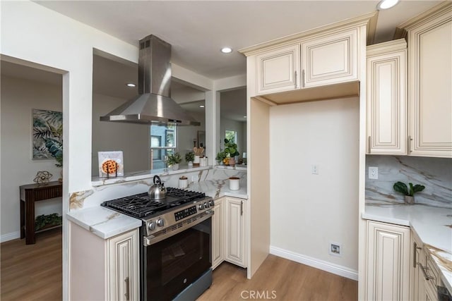 kitchen featuring light wood-style floors, stainless steel range with gas cooktop, decorative backsplash, island range hood, and cream cabinetry