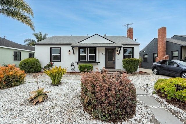bungalow-style home with roof with shingles, stucco siding, and a chimney