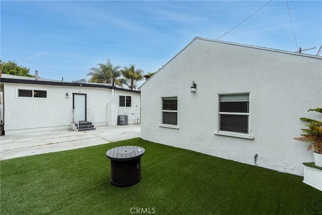 back of house with stucco siding, entry steps, cooling unit, a lawn, and a patio