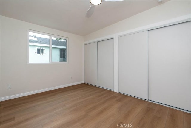 unfurnished bedroom featuring baseboards, ceiling fan, two closets, and light wood finished floors