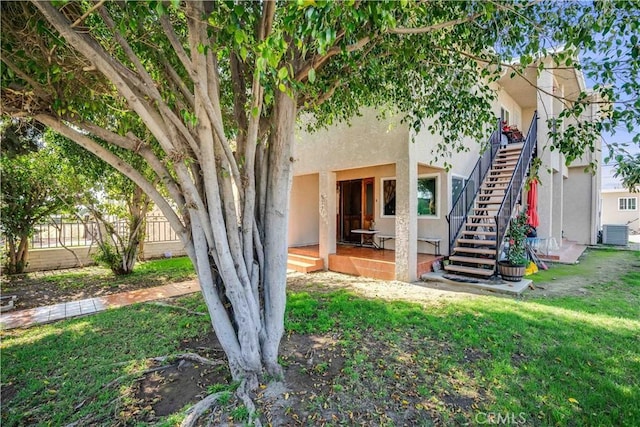 back of property with central air condition unit, stucco siding, stairs, and fence