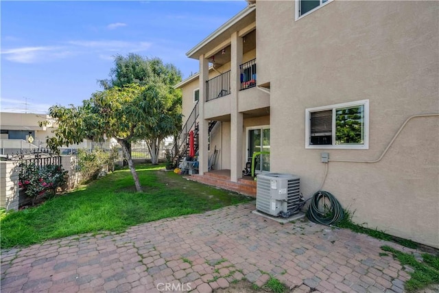 rear view of property with fence, stucco siding, central AC unit, a patio, and a yard