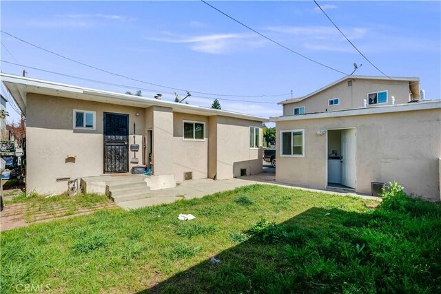 back of house featuring stucco siding and a yard