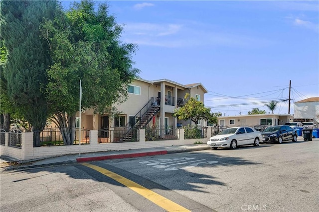 view of front facade with fence private yard, stucco siding, and stairway