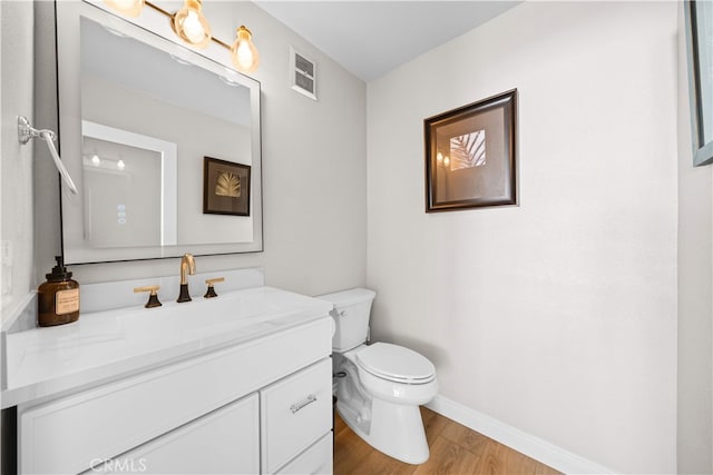 half bath featuring wood finished floors, toilet, baseboards, and vanity