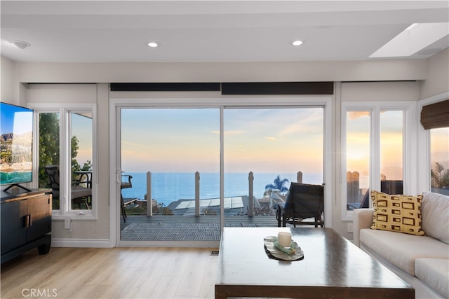 living room with a water view, wood finished floors, recessed lighting, baseboards, and a skylight