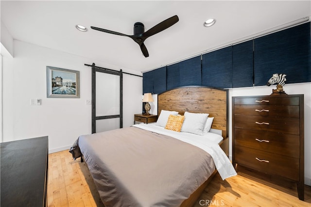 bedroom with a barn door, recessed lighting, light wood-style floors, and a ceiling fan