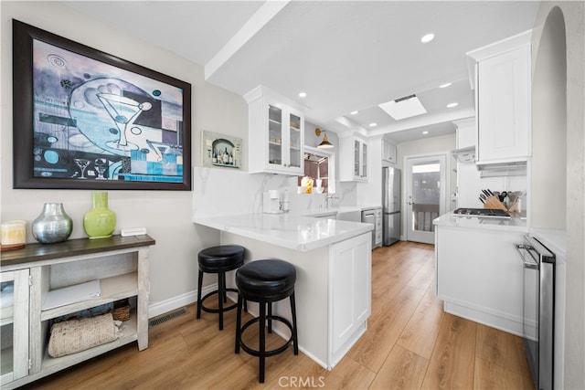 kitchen with stainless steel appliances, a skylight, white cabinets, light wood-type flooring, and recessed lighting
