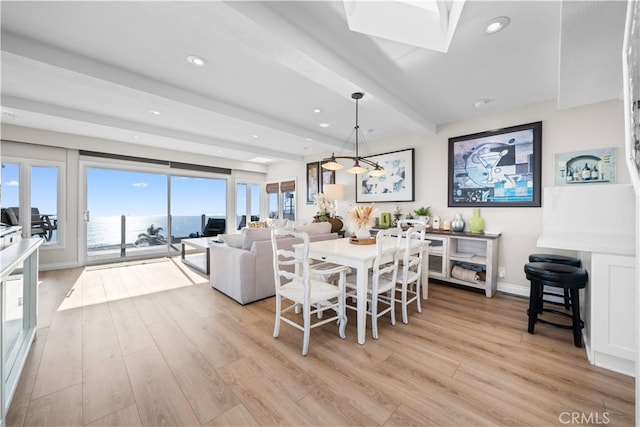 dining area with beamed ceiling, light wood-style floors, a water view, recessed lighting, and baseboards
