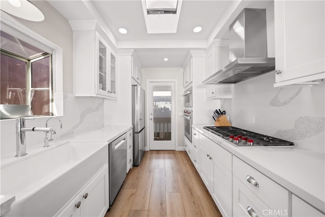kitchen featuring wall chimney exhaust hood, stainless steel appliances, recessed lighting, white cabinetry, and light countertops