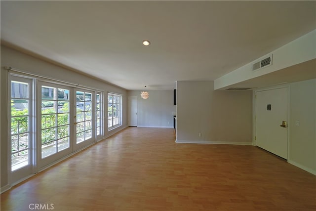 unfurnished room with an inviting chandelier, baseboards, light wood-type flooring, and visible vents
