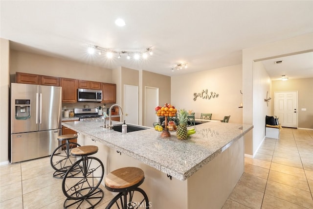 kitchen with brown cabinets, light tile patterned flooring, a breakfast bar, a sink, and stainless steel appliances