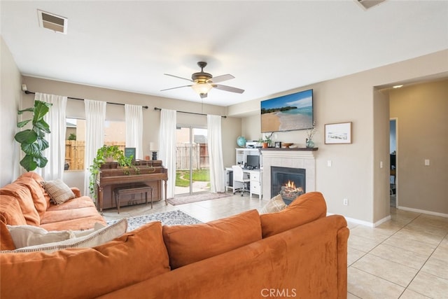 living room featuring a ceiling fan, visible vents, a tiled fireplace, light tile patterned floors, and baseboards