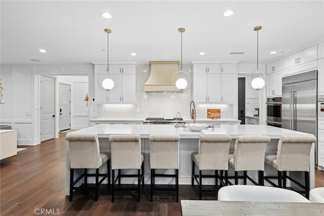 kitchen with light countertops, white cabinetry, custom range hood, a sink, and appliances with stainless steel finishes
