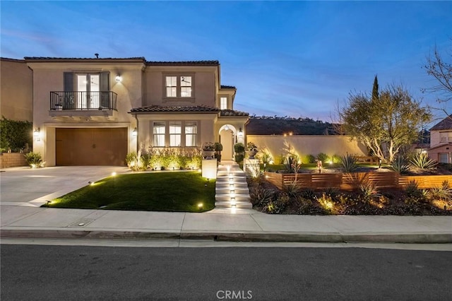 mediterranean / spanish house featuring a garage, stucco siding, a balcony, a tiled roof, and driveway