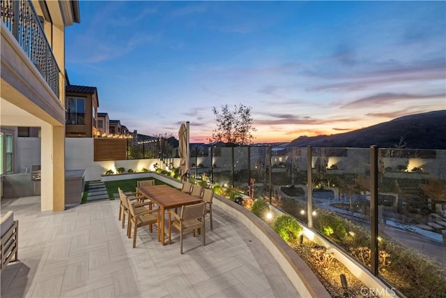 patio terrace at dusk featuring exterior kitchen, fence, and outdoor dining space