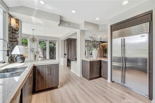 kitchen featuring dark brown cabinetry, stainless steel built in fridge, a sink, and light wood-style floors